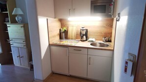 A compact kitchen with white cabinets, a microwave, a coffee maker, and a sink. - Kilian Reiter vacation apartment (Ruhpolding)