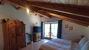 A bedroom with a wooden ceiling, a bed, a TV, a wardrobe, and a window with curtains. - Kilian Reiter vacation apartment (Ruhpolding)