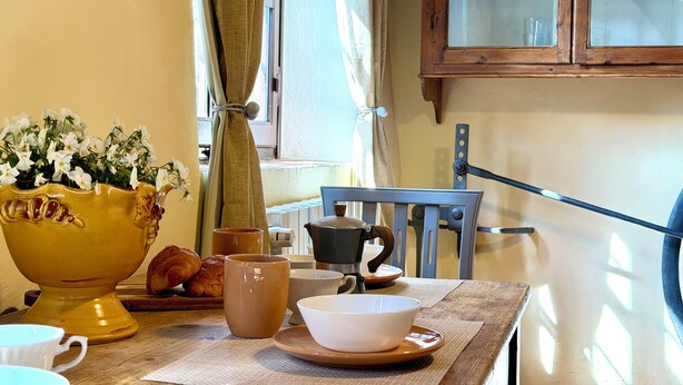 Et spisebord med en vase med blomster, kaffemaskine samt diverse kopper og tallerkener.