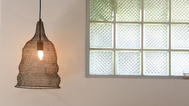 Een keuken met een hangende hanglamp, een raam met glas-in-lood, een spoelbak met kraan en een plant in pot.