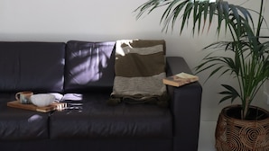Een donkere leren bank met een geweven plaid, een houten dienblad met een kom en mok, en een potplant.