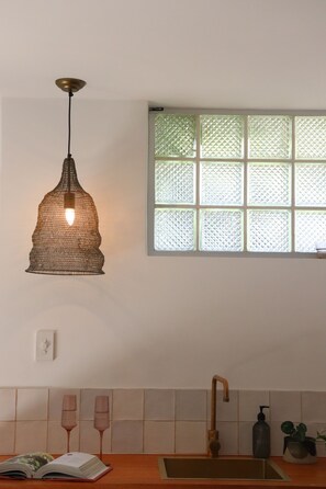 Een keuken met een hangende hanglamp, een raam met glas-in-lood, een spoelbak met kraan en een plant in pot.