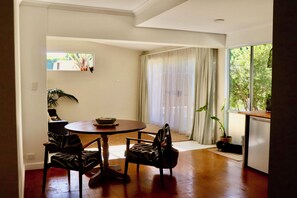 Un comedor con una mesa redonda, cuatro sillas, una ventana con cortinas y una planta en maceta.