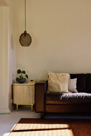 Een woonkamer met een donkerbruine bank, een witte plaid en een hanglamp.