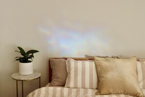 Una cama con ropa de cama a rayas, una planta en maceta sobre una mesita de noche y una pared con una proyección de luz.