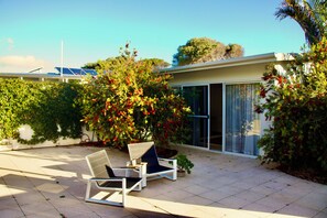 A modern house with a patio, two lounge chairs, a small tree, and a solar panel array.