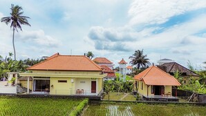 A traditional house with a tiled roof, surrounded by a water body and greenery. - Puri Prana Villa (Ubud)