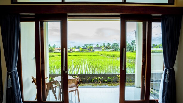 A room with a view of a green field through a sliding glass door. - Puri Prana Villa (Ubud)