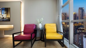 Una habitación moderna con dos sillones, una mesita, un florero con flores y un ventanal con vista a la ciudad.
