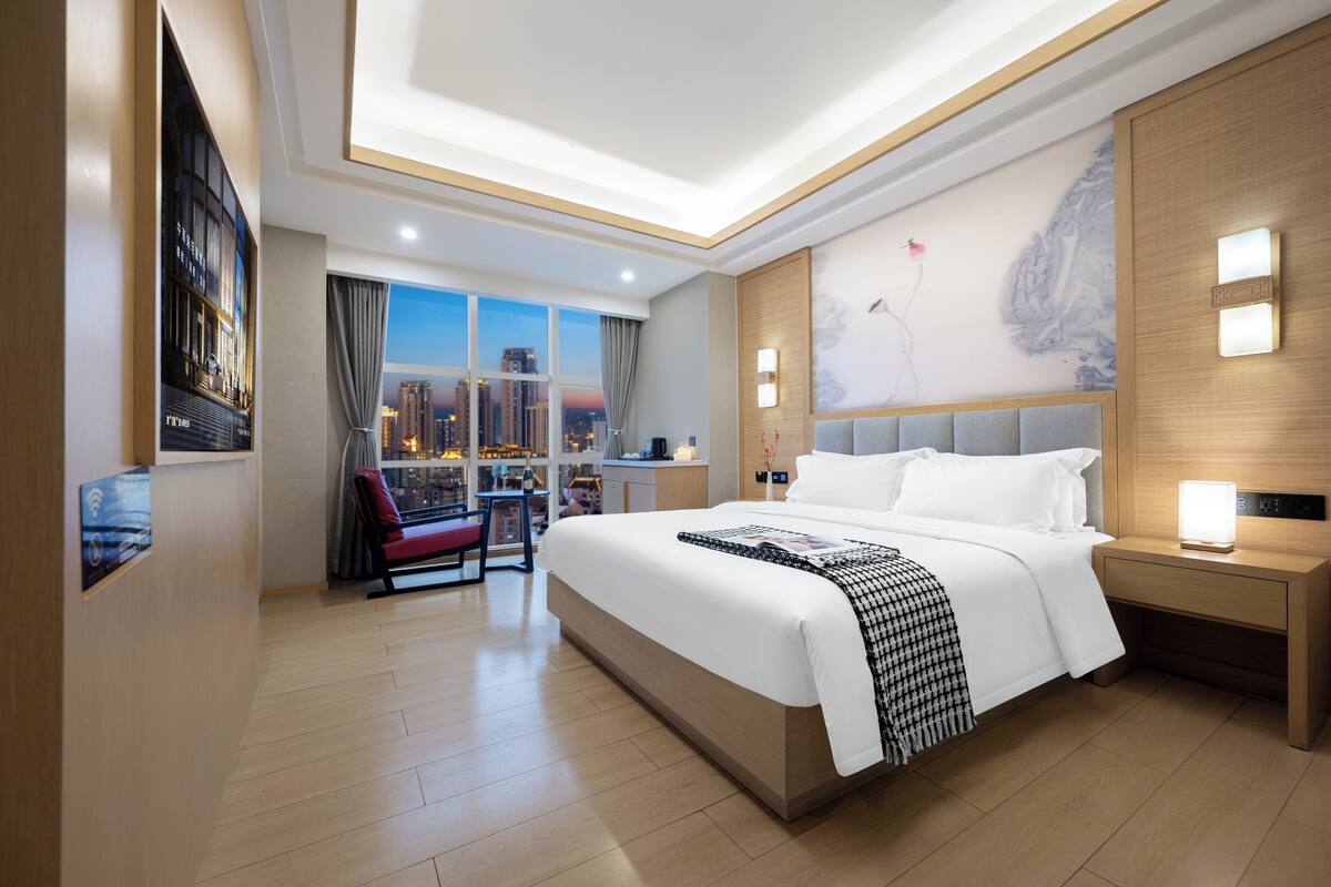 Une chambre d’hôtel moderne, dotée d’un grand lit, d’un bureau, d’une chaise et offrant une vue sur le paysage urbain par la fenêtre.