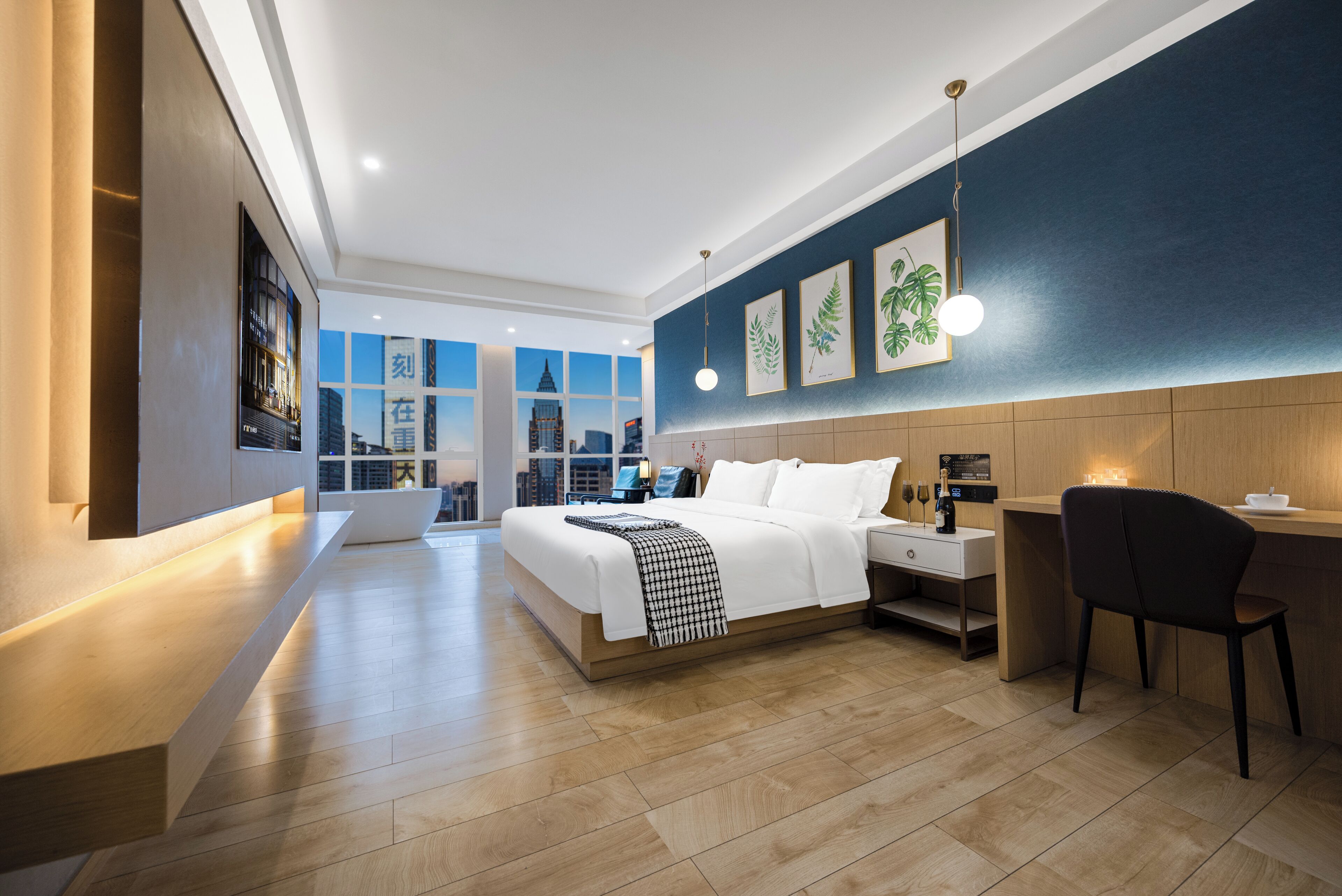 A modern hotel room with a large bed, bedside table, desk, and chair.