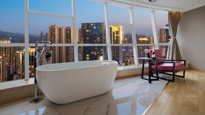 Un baño moderno con una bañera independiente, una silla y una mesa con una botella.