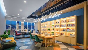 A modern lounge area with a checkered floor, a central wooden table, green chairs, and a bookshelf with various items. - Chongqing Meishu Tianqing Skyview Hotel  (Chongqing)