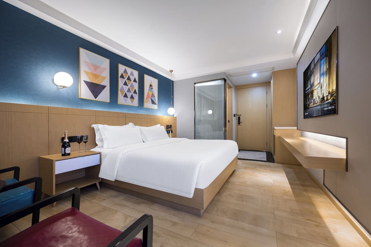 Une chambre d’hôtel moderne, équipée d’un lit, d’une table de chevet, d’œuvres d’art murales et d’une porte de salle de bain.
