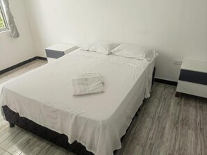 Een net opgemaakt bed met een witte spreideken en kussens, een nachtkastje en een bijzettafeltje.
