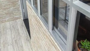 Un bâtiment moderne doté de grandes fenêtres, d’un mur à texture et d’une plante en pot posée sur le rebord de la fenêtre.