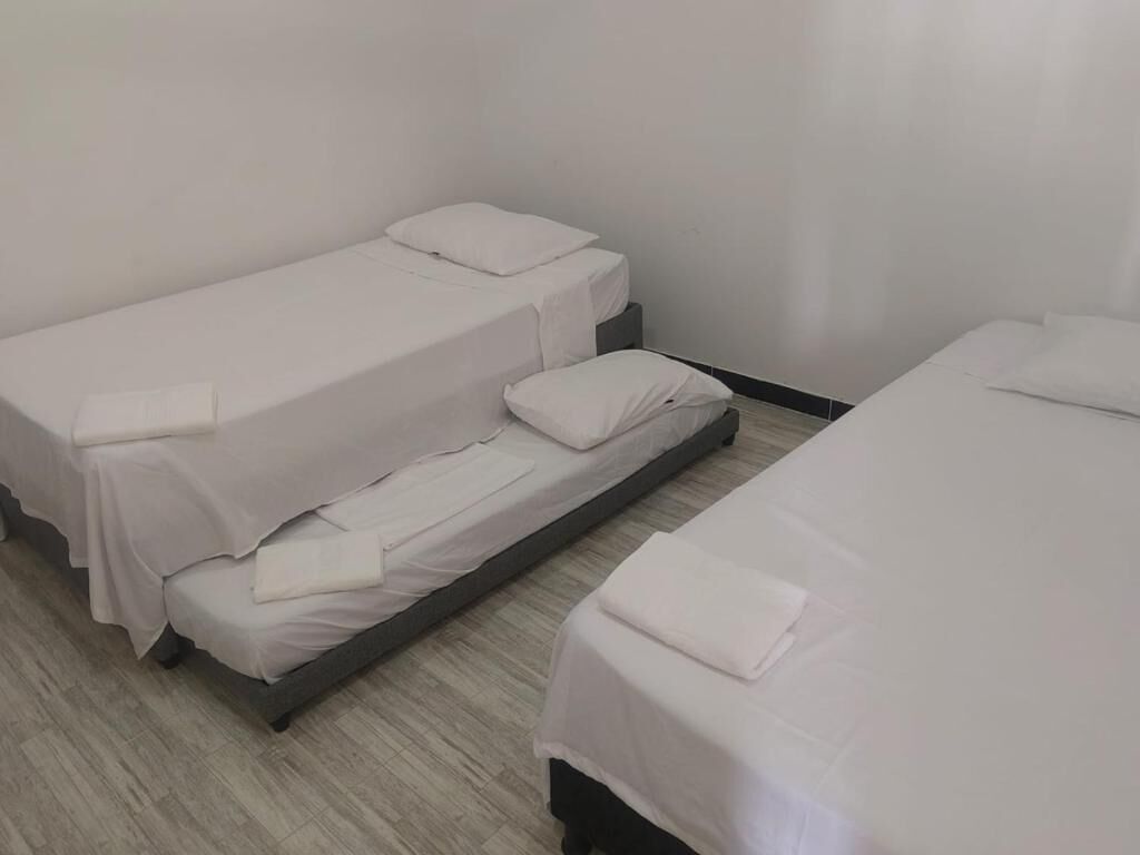 Ein Zimmer mit drei Einzelbetten, die in einer Reihe angeordnet sind, jeweils mit weißer Matratze und Kissen.