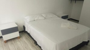 Un lit bien fait, avec une literie blanche, une table de chevet et une petite table à poser près du lit.