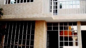 Un immeuble à plusieurs étages avec des fenêtres grillagées, un balcon et un intérieur visible, dans lequel on aperçoit un objet rouge.