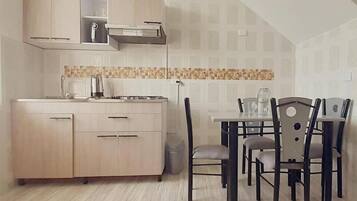 A compact kitchen with a dining area, wooden cabinets, a tiled backsplash, and a small trash bin.