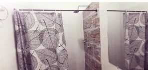 Een badkamer met douchegordijn met bladmotief, een stenen muur en een spiegel.