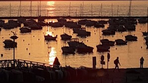 Solnedgang over en lysthavn med fortøjede både og folk, der går langs stranden.