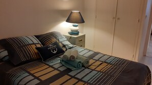 En pænt redt seng med stribet sengetøj, en pude med et maritimt ankerdesign og en sengetøjslampe.