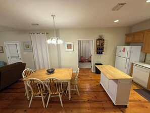 Una cocina con armarios de madera, un refrigerador, un lavavajillas y un comedor con una mesa y sillas.