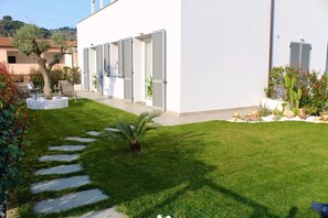 A modern building with a white exterior, a well-maintained lawn, and a stone pathway leading to the entrance. - Relaxation in private garden, outdoor kitchen, private parking lot (Diano Castello)