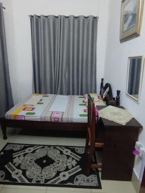 Een slaapkamer met een bed, een bureau, een stoel, een vloerkleed en gordijnen.