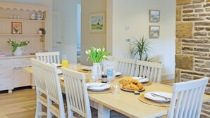 Un comedor con una mesa de madera, sillas blancas y una pared de piedra.
