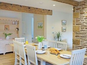 A dining area with a wooden table, white chairs, and a stone wall. - 4 bedroom accommodation in Skipton (Skipton)