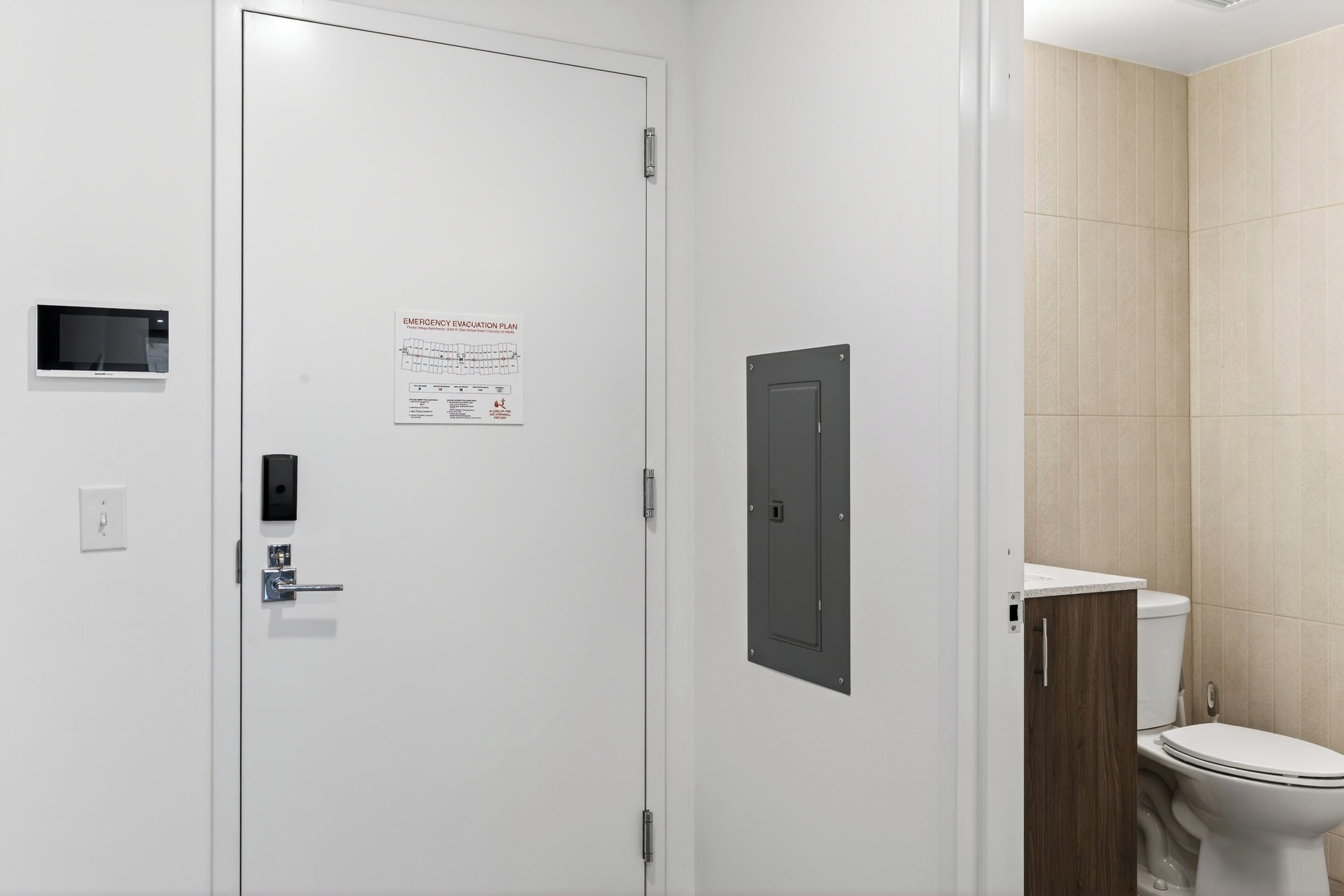 A white door with an emergency evacuation plan, a small control panel, and a wooden cabinet.