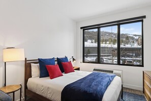 Ein Hotelzimmer mit Bett, Fenster mit Blick auf eine verschneite Landschaft, einer Lampe und einem Heizgerät.