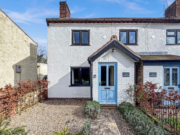Une maison à deux étages avec une porte bleue, portant le numéro 15, et un petit jardin agrémenté de gravier et d’arbustes.