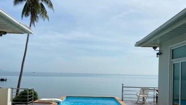 A rectangular swimming pool with a wooden deck, a palm tree, and a view of the sea. - Sook Beach House, Paknam Chumphon (Tambon Pak Nam)