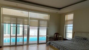 A bedroom with a bed, a chair, a table, and a view of a swimming pool through large glass doors. - Sook Beach House, Paknam Chumphon (Tambon Pak Nam)