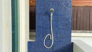 A small, enclosed shower area with blue mosaic tiles, a showerhead, and a wooden fence in the background. - Sook Beach House, Paknam Chumphon (Tambon Pak Nam)