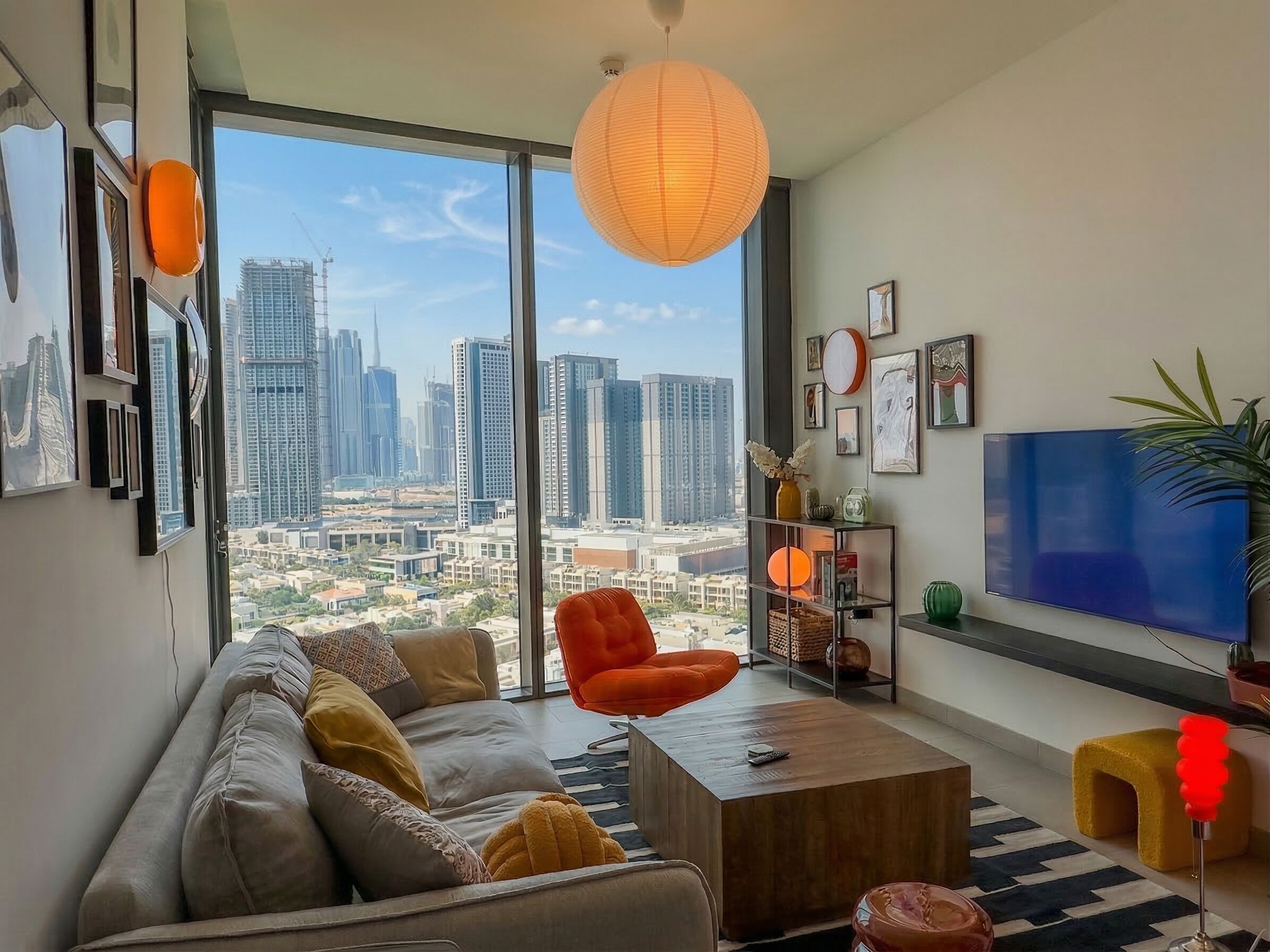 A modern living room with a sofa, a coffee table, a TV, and a view of a cityscape through large windows.