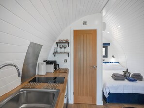 Eine kompakte, moderne Küche mit Spüle, Herd und Stauraum, die in einen Schlafbereich mit Bett und Fenster übergeht.