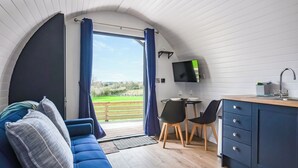 Ett mysigt rum med en blå soffa, en liten matplats med två stolar, en tv som är monterad på väggen och utsikt över omgivningarna.