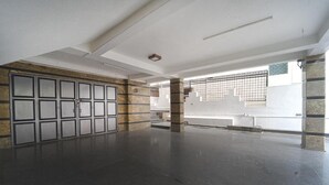 Ein geräumiger, leerer Raum mit Fliesenboden, einem großen Fenster mit Metallgitter und einer Tür mit Milchglasverkleidungen.