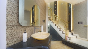 Ein Badezimmer mit einem großen Spiegel, einem Haubenspültisch, einem Handtuchspender und einer Treppe mit goldener Geländer.
