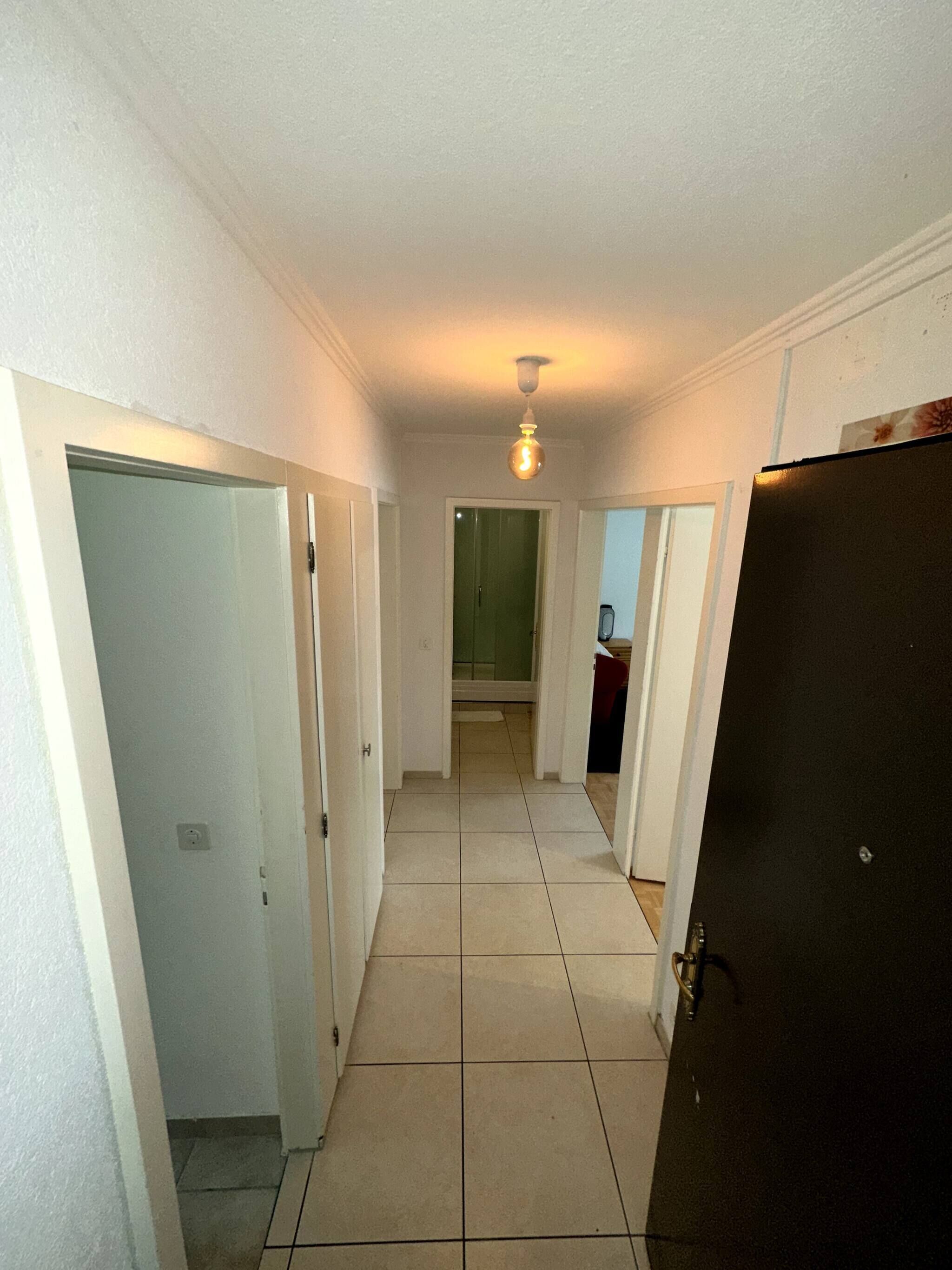 A hallway with white walls, a tiled floor, and a ceiling light fixture.