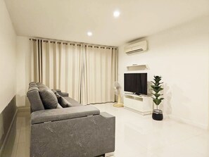 Una sala de estar moderna con un sofá, un televisor, un aire acondicionado y una planta en maceta.