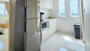 Une cuisine moderne équipée d’un réfrigérateur en acier inoxydable, d’un four à micro-ondes et d’un petit évier. Les meubles sont blancs et il y a une fenêtre avec vue.