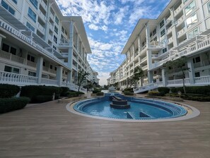 Un hotel con piscina central, varios balcones y cielo despejado.