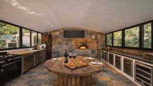 A modern kitchen with a stone wall, a built-in oven, and a round wooden table set for dining. - Luxury villa Lilly Aaron swimming pool and lake of sainte croix (Artigues)