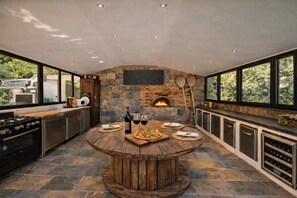 A modern kitchen with a stone wall, a built-in oven, and a round wooden table set for dining. - Luxury villa Lilly Aaron swimming pool and lake of sainte croix (Artigues)