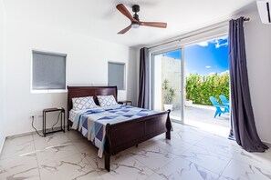 A bedroom with a bed, a ceiling fan, a window with blinds, a small table, and a view of the outside. - Private Sosua Villa, Pool, BBQ, Sosua Ocean Village (Sosúa)